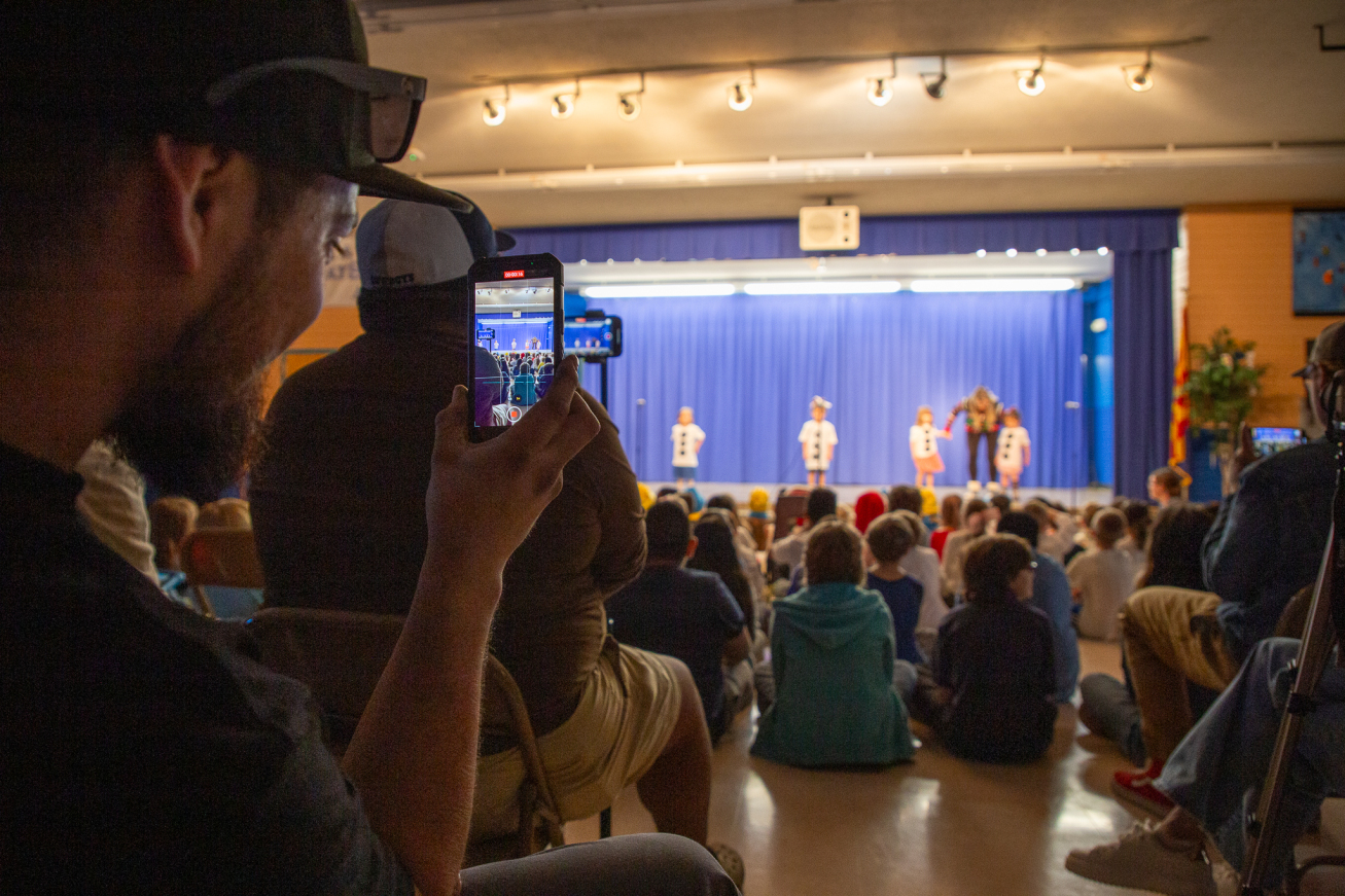 A parent takes a cell phone video of their child on stage.