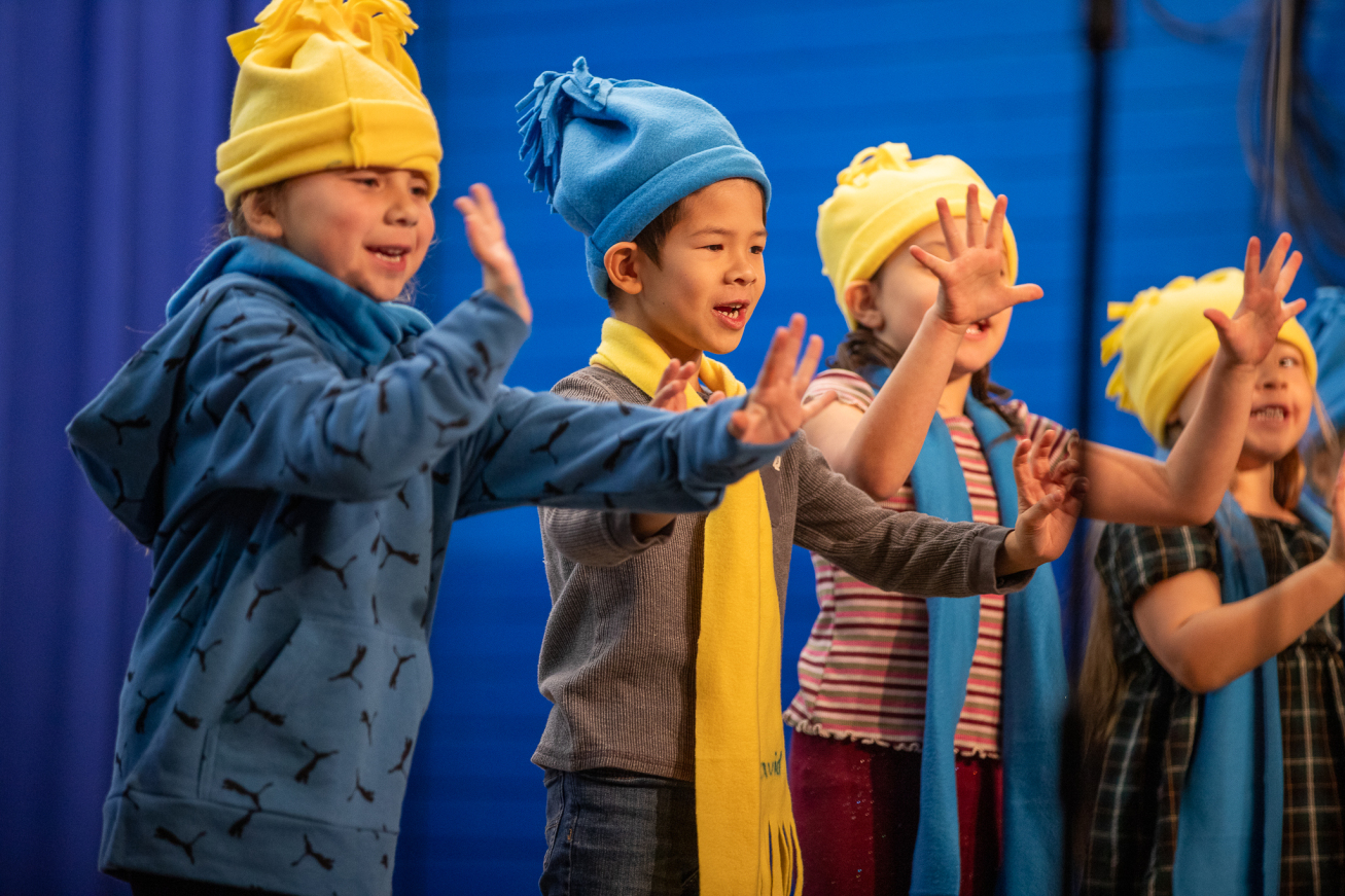 Students decked out in blue and yellow hats and scarves perform on stage