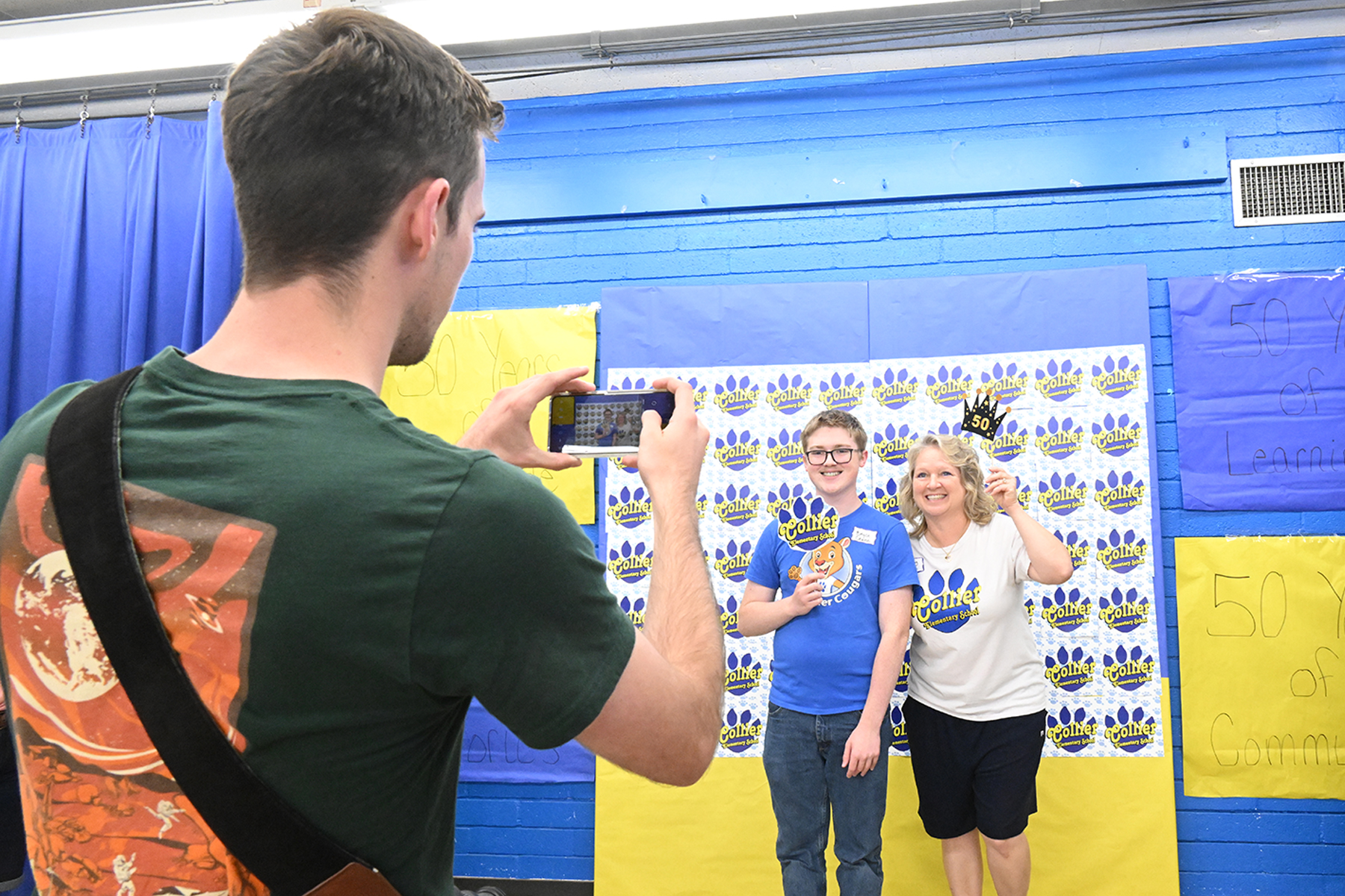 A former student and his mom pose in front of the Collier backdrop