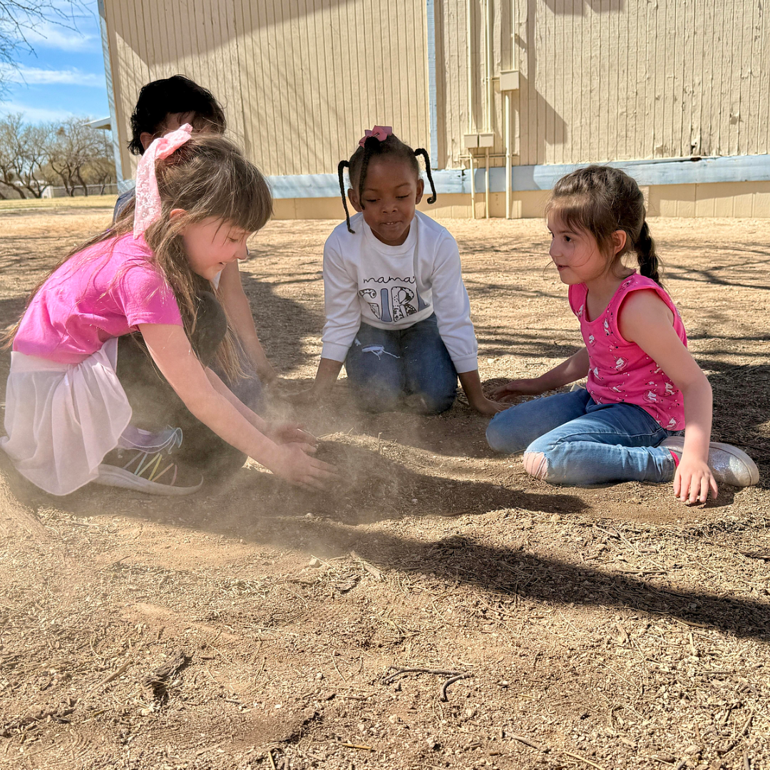 Four young girls play in the dirt together