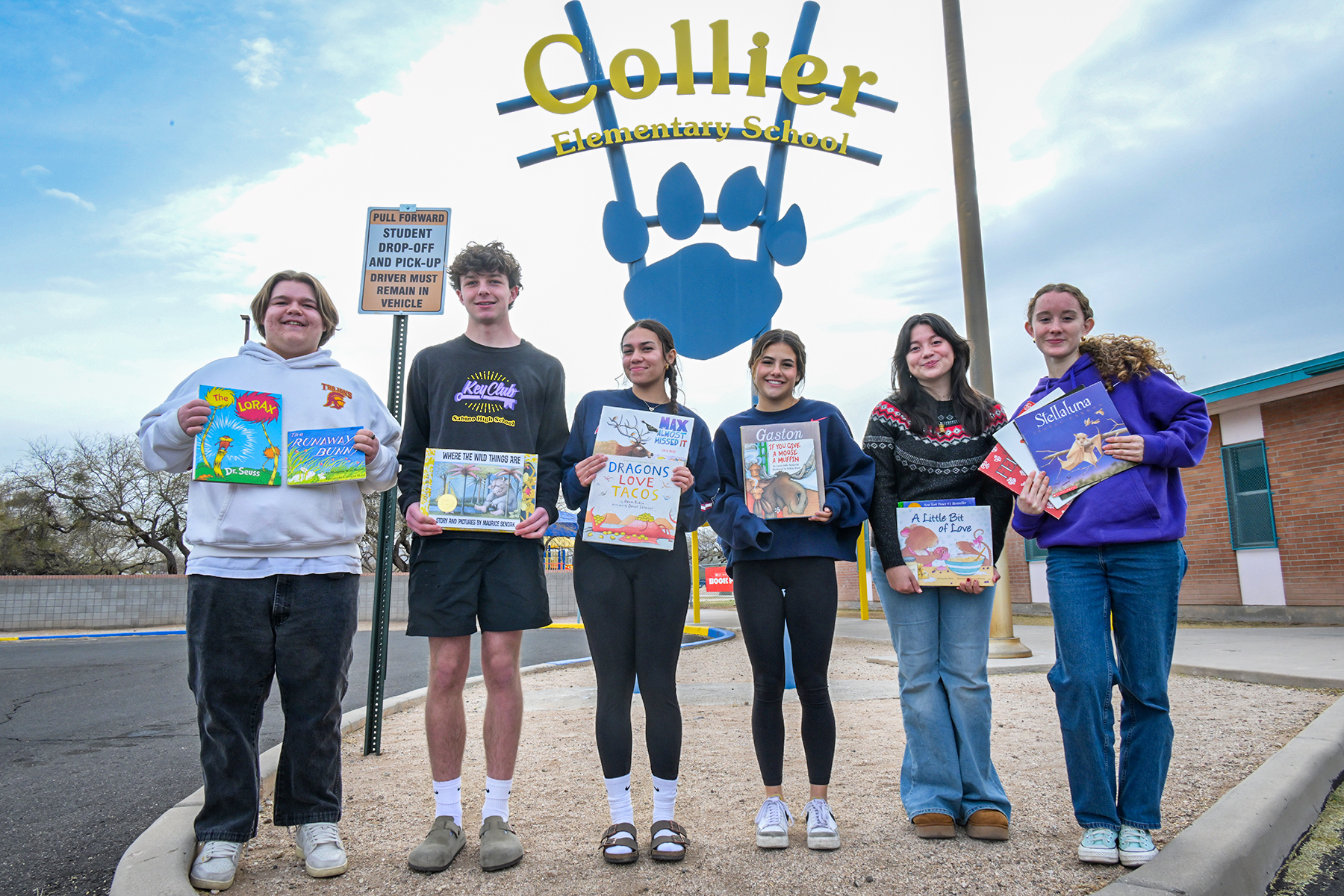 Six high school students stand outside Collier Elementary holding books