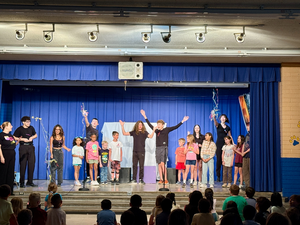 High school students pose on stage with elementary students