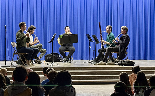 A wind instrument quartet performs for students