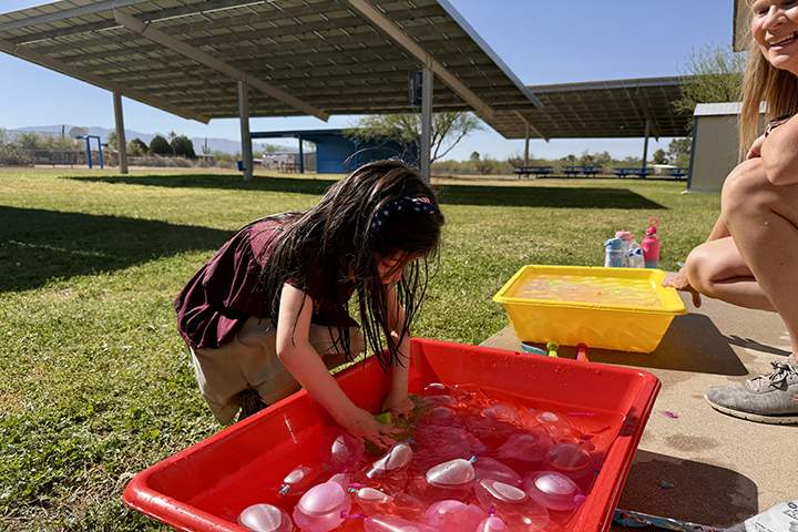 A little girl reaches into a red container to pick out a water balloon