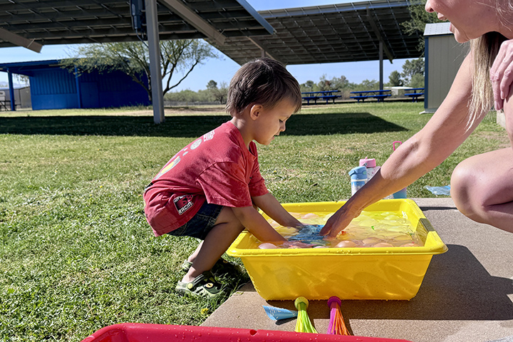 A little boy reaches into a yellow container for a water balloon