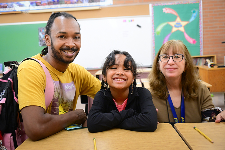 A girl poses with her dad and her new teacher on the first day of school