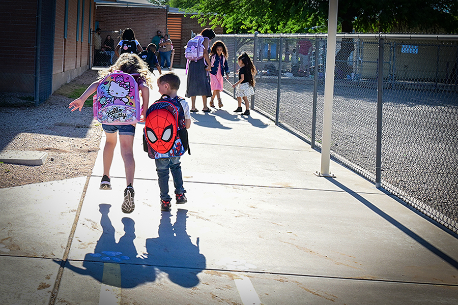 A little girl and little boy walk into school with their backpacks