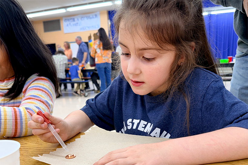 A girl uses an eyedropper to put a drop of water on a penny
