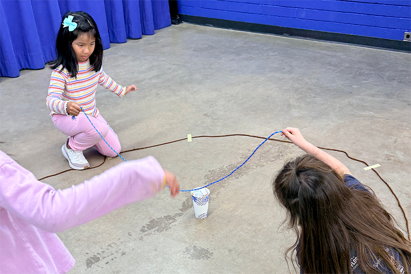 Three girls hold wires over a cup