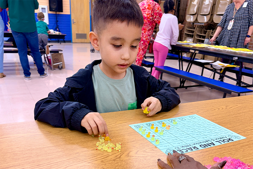A little boy plays a game with dice and tiny plastic ducks