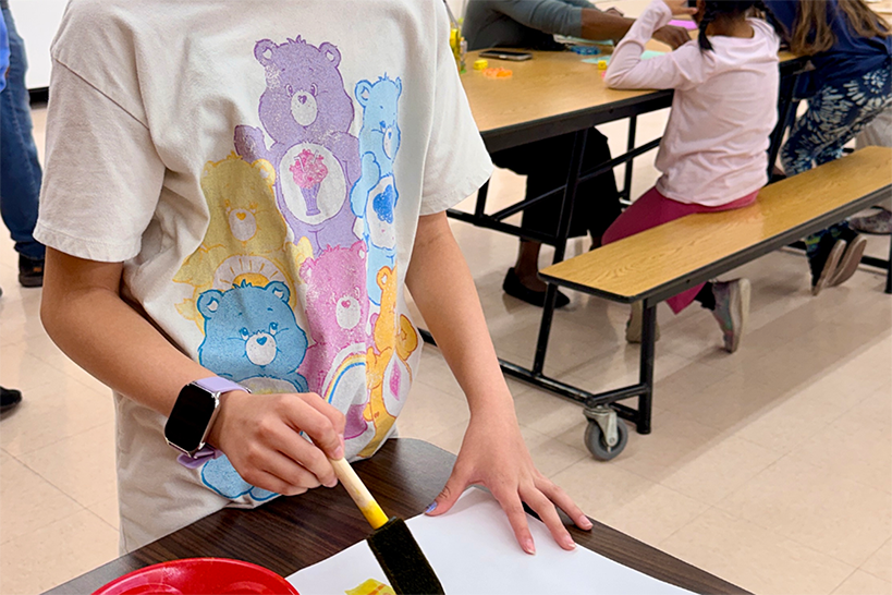 A girl in a Care Bears shirt paints a piece of paper