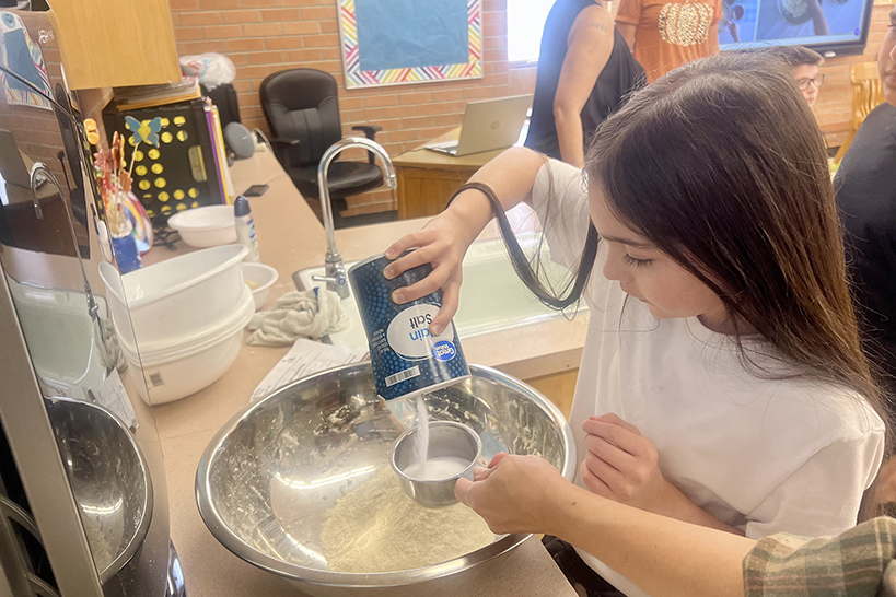 A girl pours salt into her bowl of masa dough
