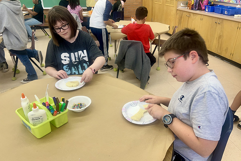 A boy and girl sit at a table and create their masa dough sculptures