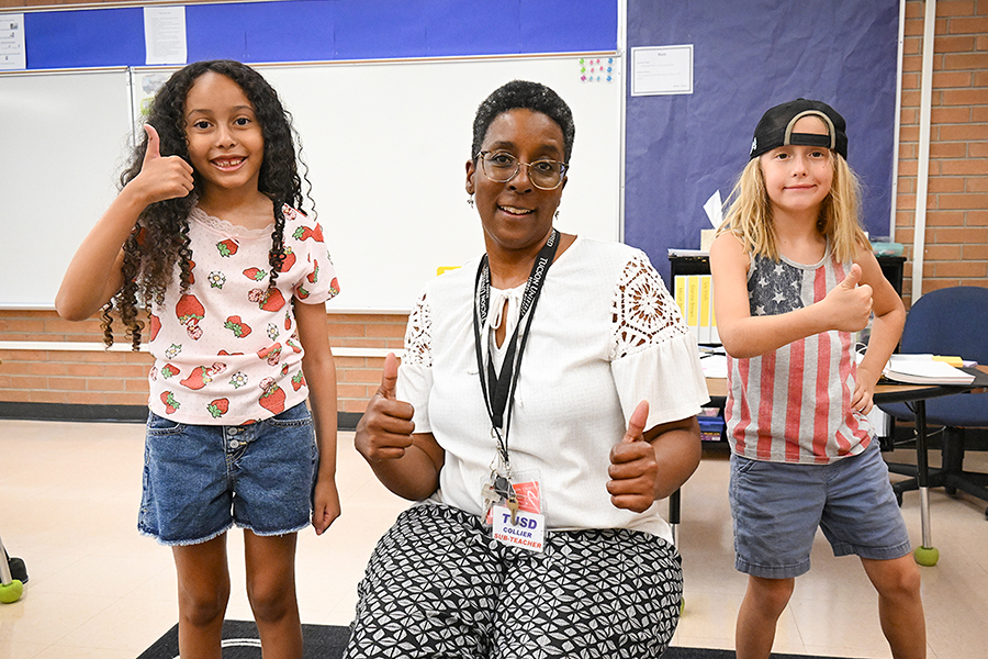 Two girls and their teacher give a thumbs up in the classroom