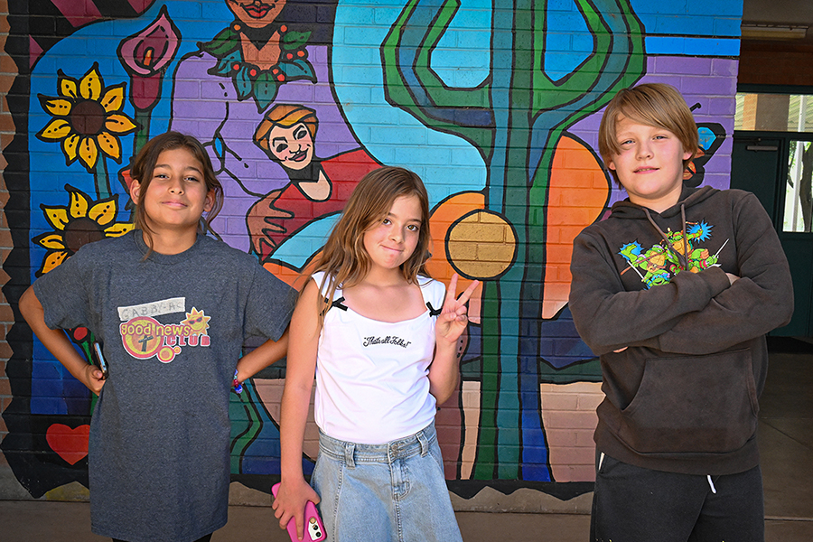 Two girls and a boy pose in front of a colorful mural