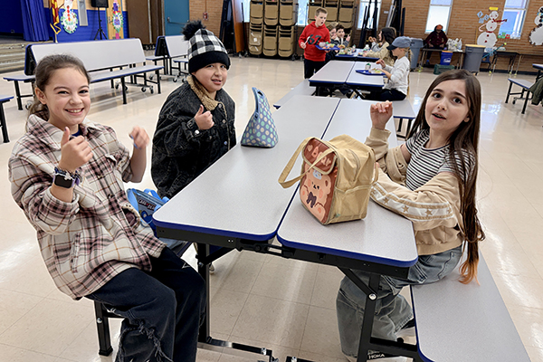 Three students give a thumbs up sitting at the new cafeteria table