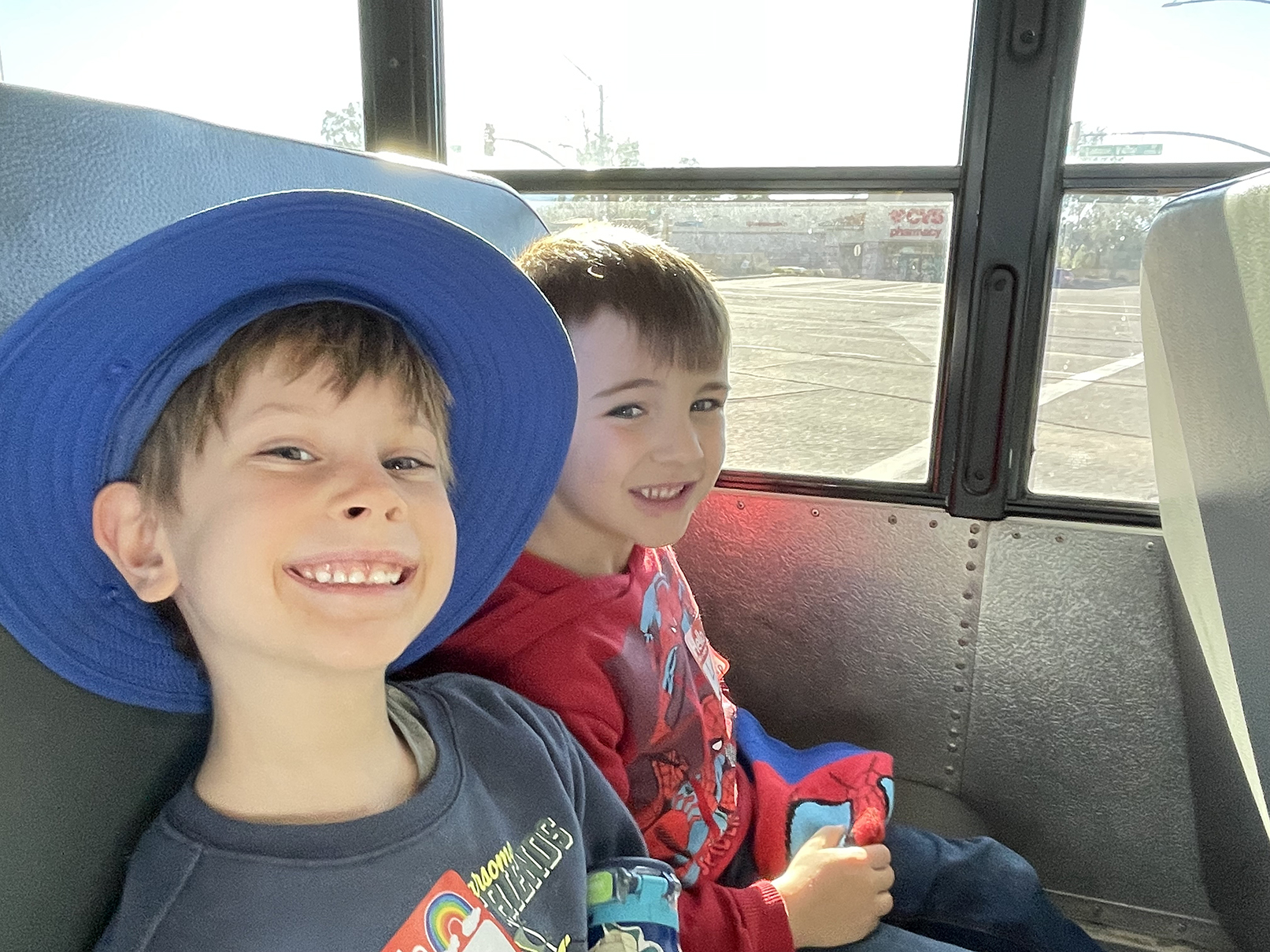 Two little boys smile from their school bus seat