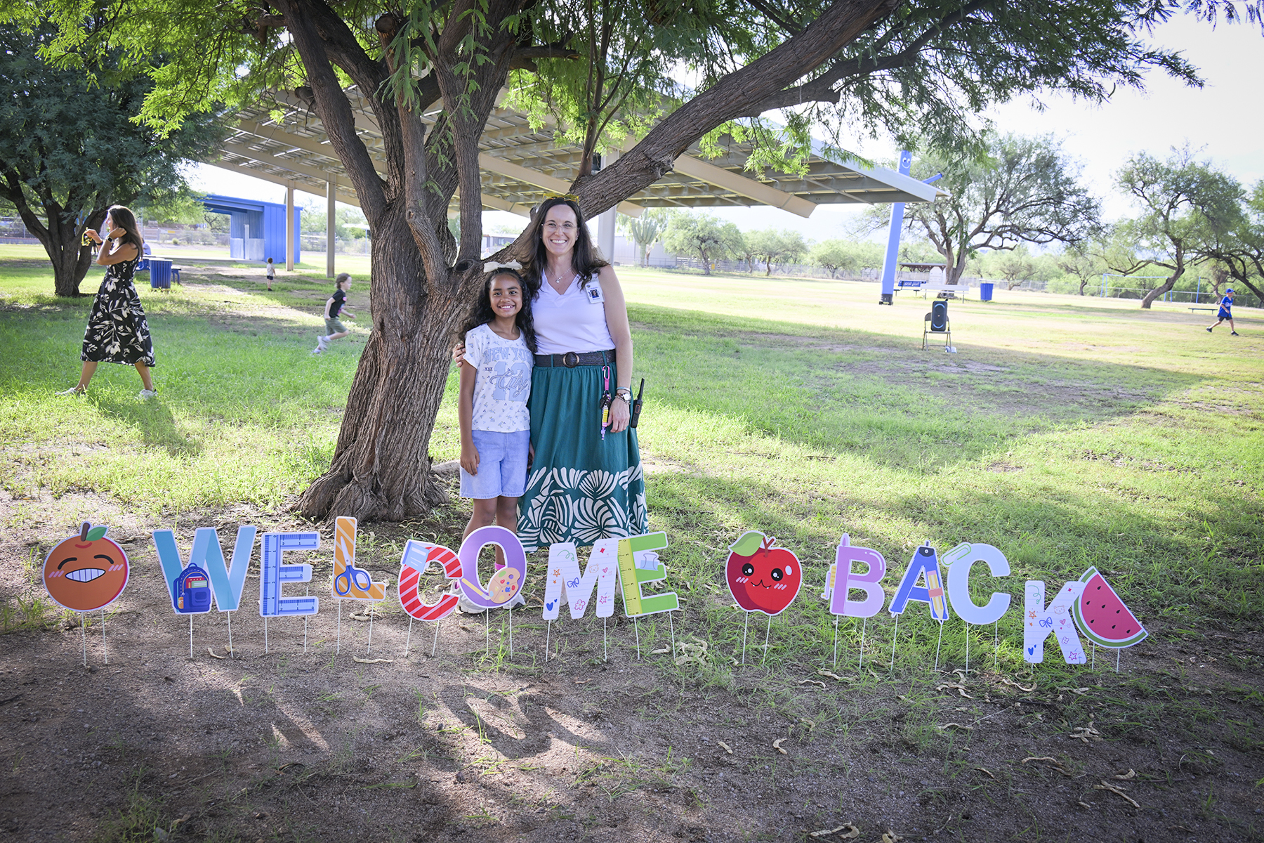 A girl and the principal smile on the field behind letters reading Welcome Back