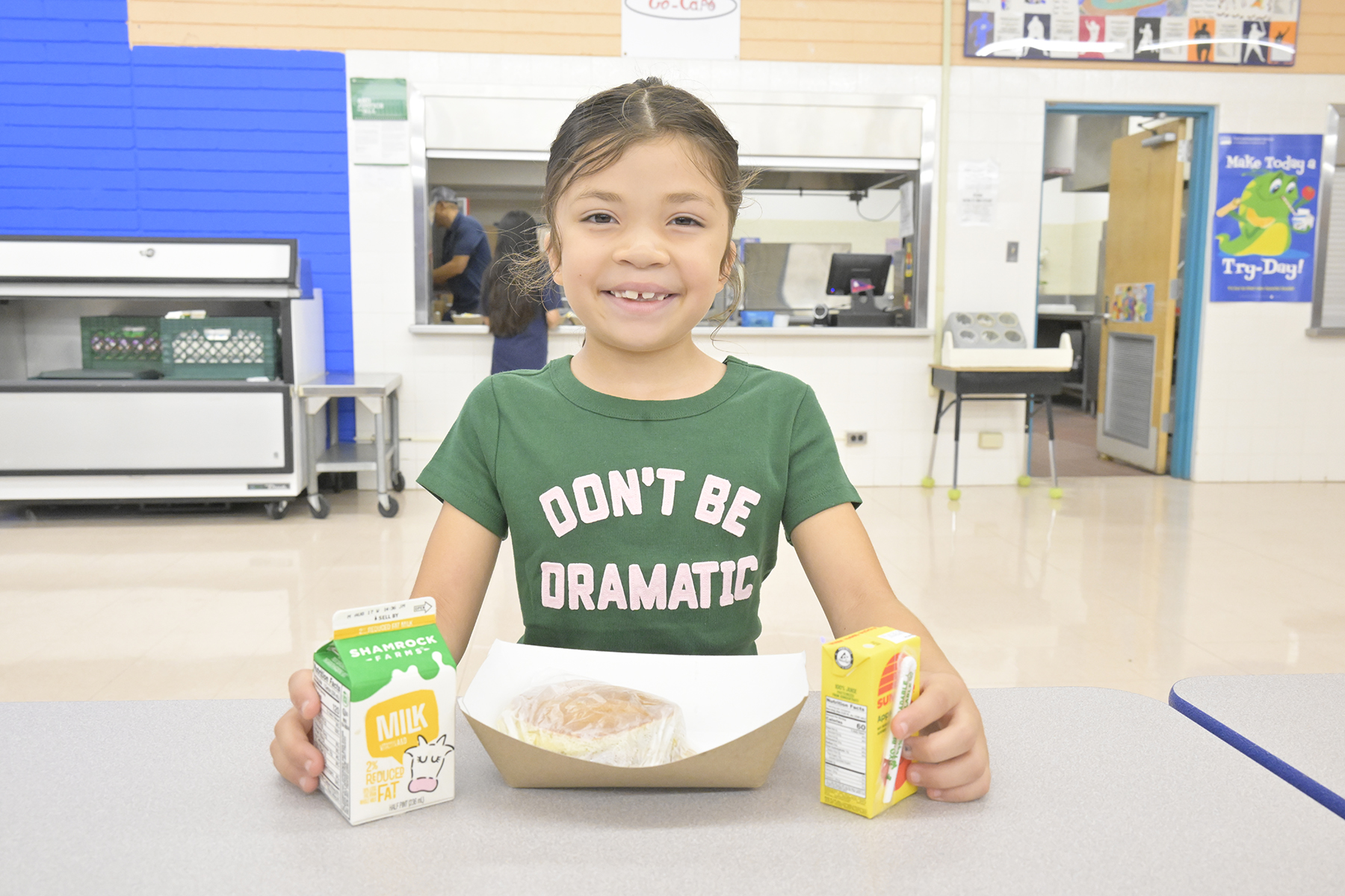 A girl smiles in the cafeteria with her breakfast