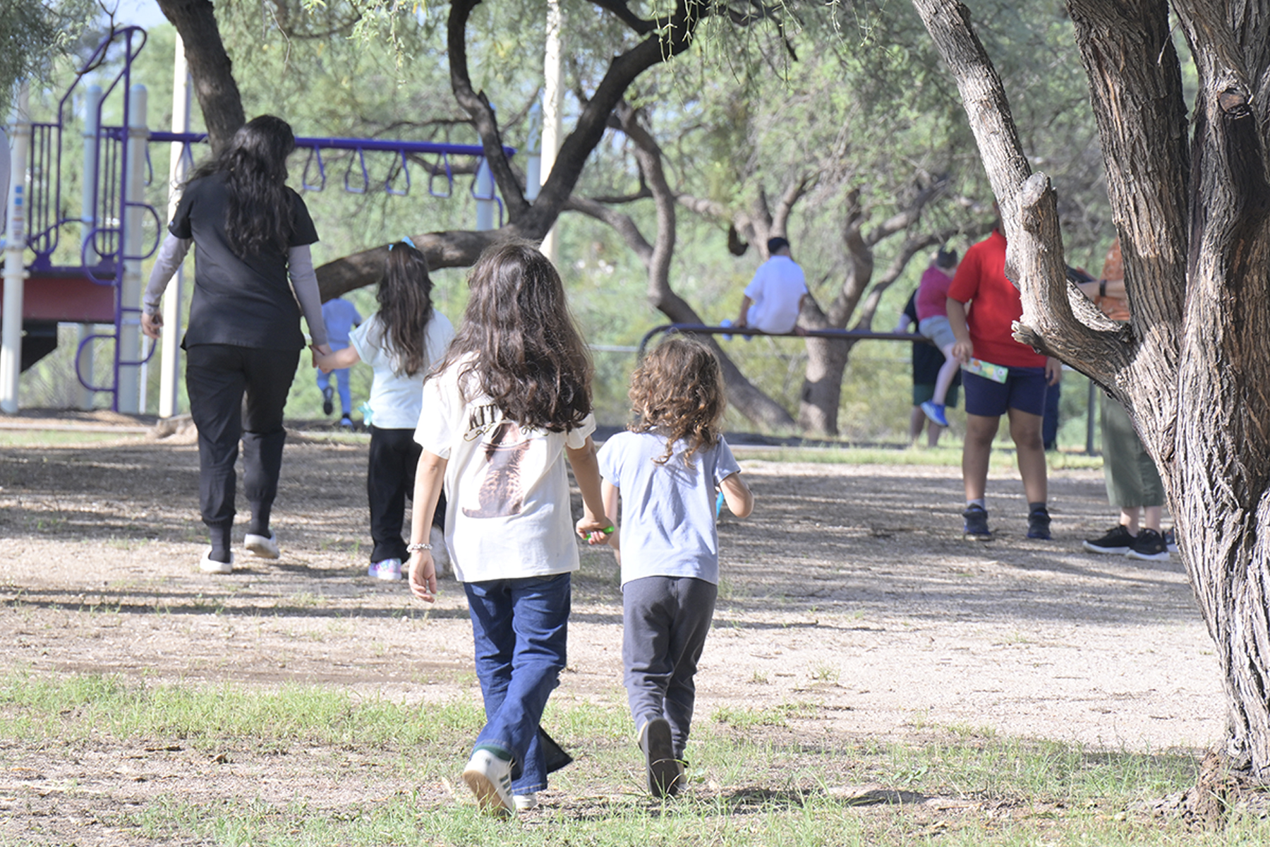 Two young siblings walk together to the playground